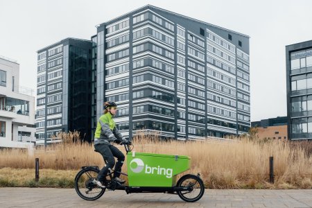 Bringbud på grøn elcykel transporterer pakker i et boligområde.