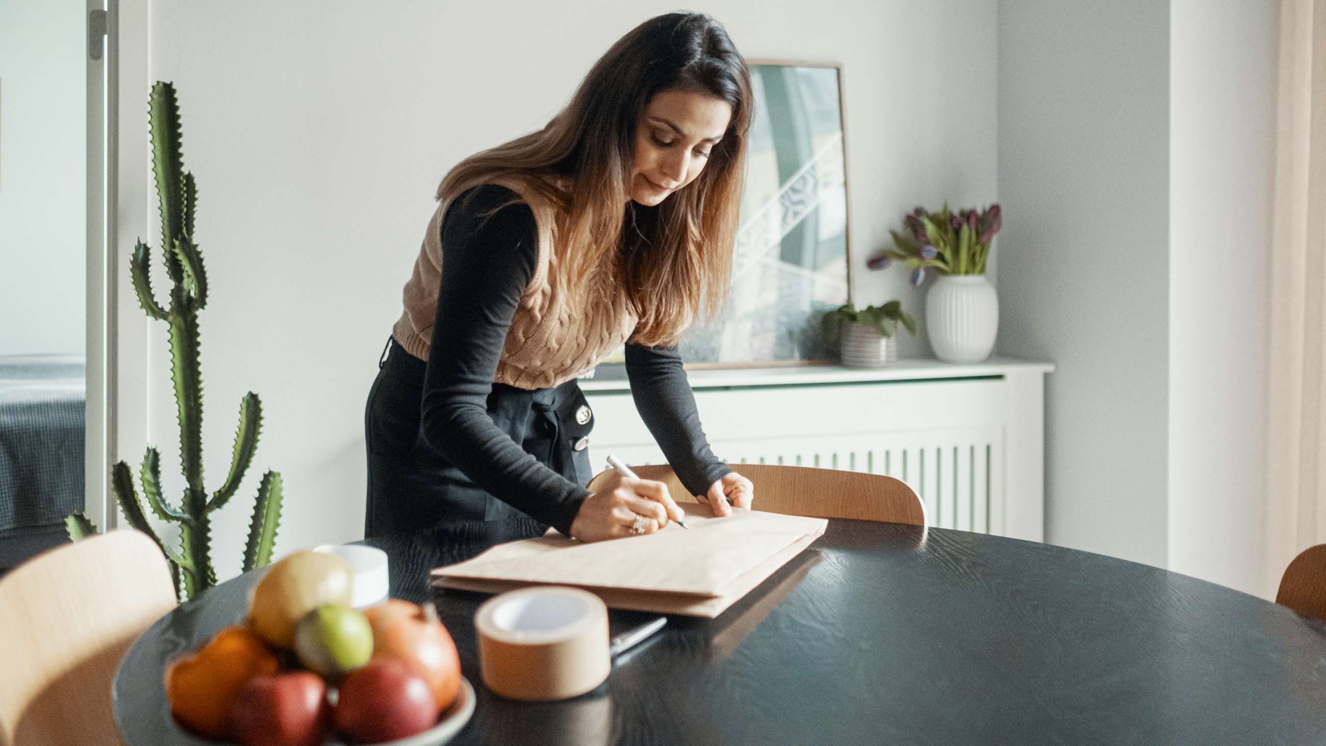 En kvinde læner sig over et bord og skriver på en pakke.