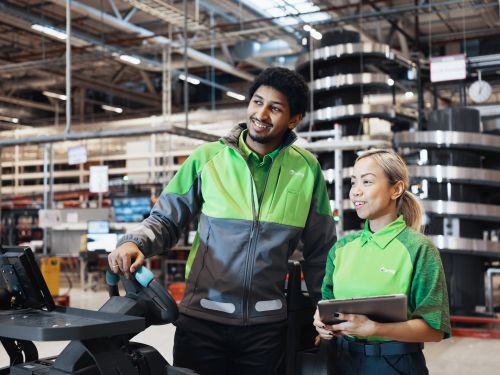 To Bring-kolleger står smilende ved siden af ​​hinanden på et lager