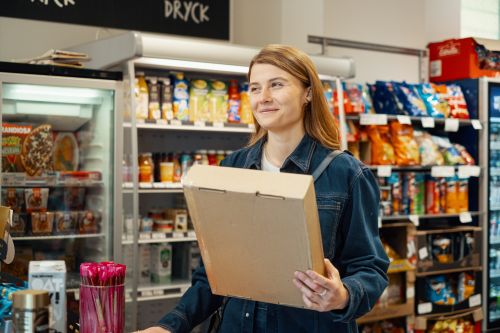 En kvinde står med en pakke i hånden på en pakkeshop