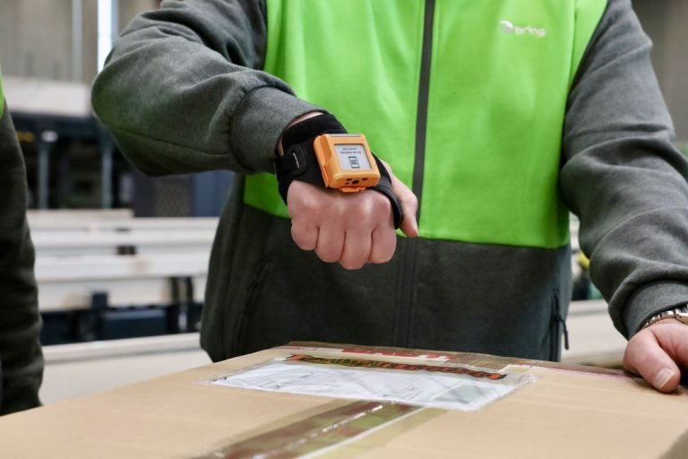 En mand i Bring tøj, som har en ProGlove på hånden ved scanning af en pakke