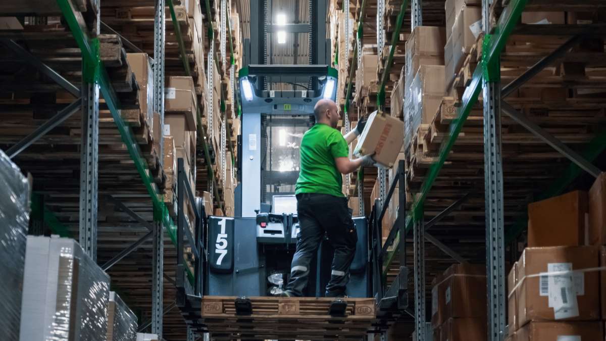En mand samler pakker fra et lager stående på en gaffeltruck