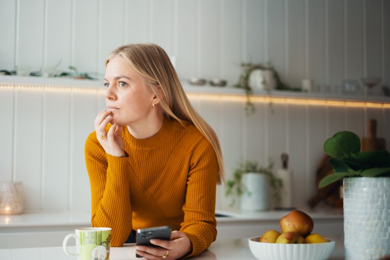 En kvinde står ved en bænk med en telefon i hånden og ser eftertænksom ud