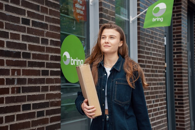 Pige står foran en Bring pakkeshop for at hente eller sende en pakke.