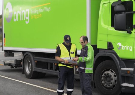 En chauffør i samtale med en tolder foran en Bring lastbil